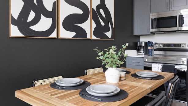 Una cocina moderna con gabinetes grises, electrodomésticos de acero inoxidable y una mesa de comedor de madera dispuesta con platos y una planta en maceta.