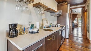 A kitchen with a built-in dishwasher, a coffee maker, and a sink. There are shelves above the counter holding glasses and a kettle. - Riverwalk Sunsets - On the Water (Wilmington)