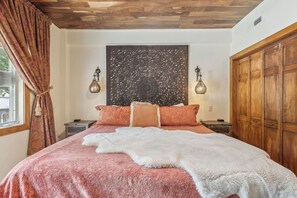 A bedroom with a large bed, a decorative headboard, two bedside lamps, and a wooden wardrobe.