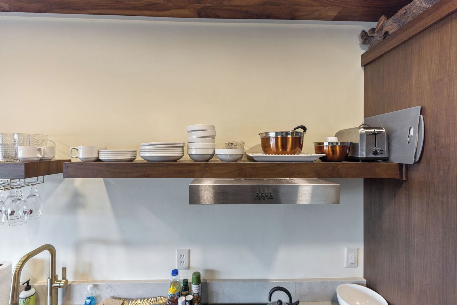 Una cocina con un extractor de acero inoxidable, un tostador y varios platos en un estante de madera.