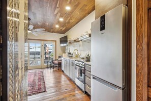 A modern kitchen with a stainless steel refrigerator, wooden ceiling, and a view to the outside.