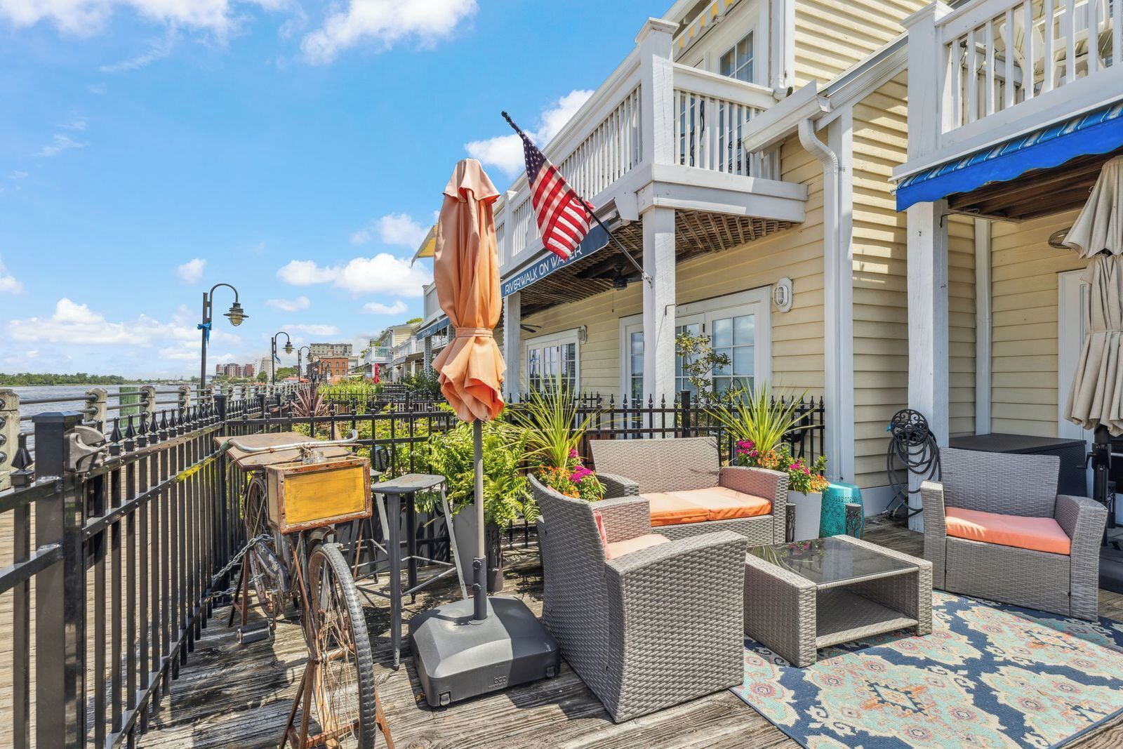 A waterfront patio with outdoor seating, an American flag, and a view of the river.