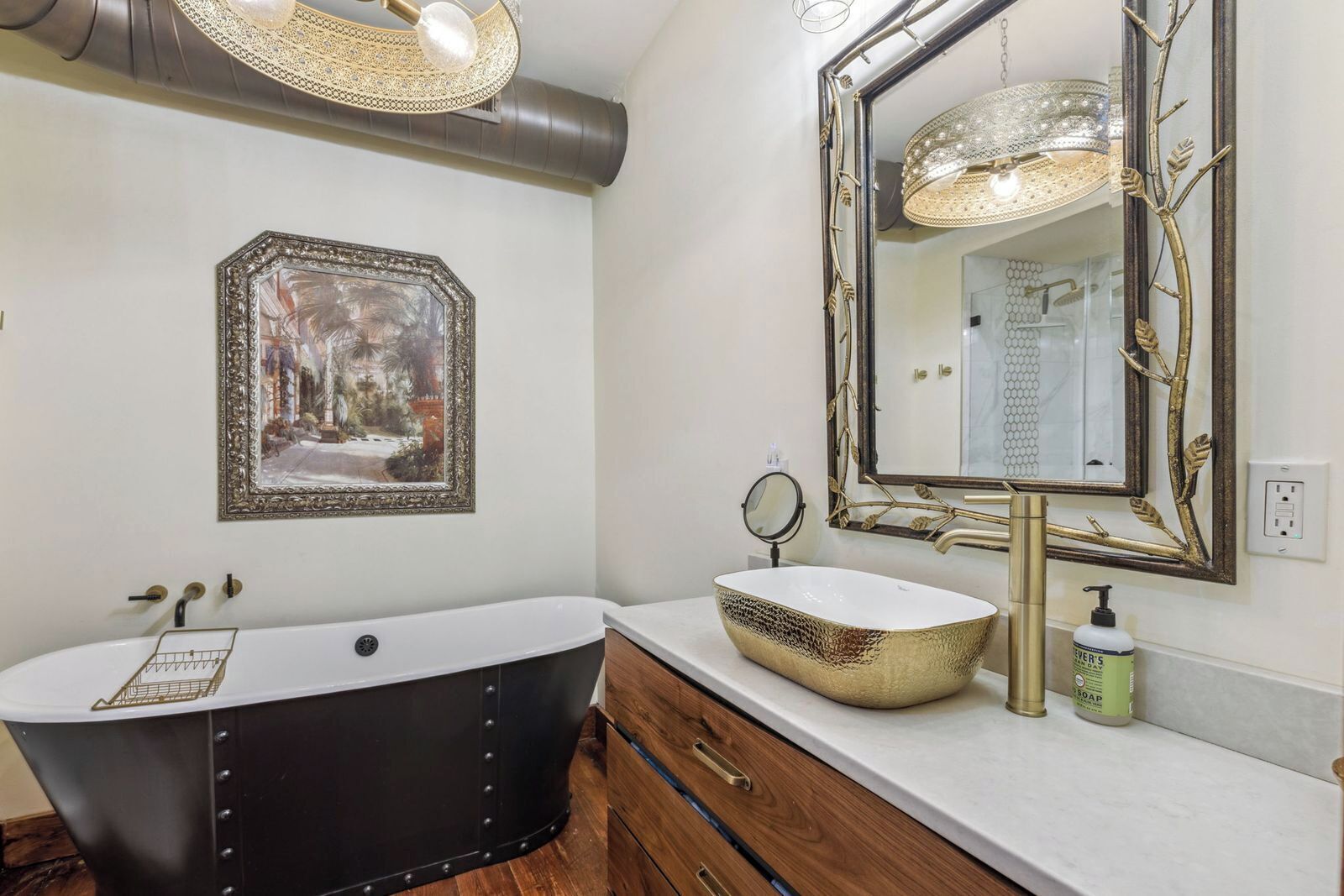 Un bagno con una vasca freestanding, uno specchio grande con cornice decorativa e un lavandino con lavabo dorato.
