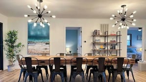 A dining area with a wooden table and chairs, two pendant lights, a bookshelf, and a painting on the wall. - A Wave From It all - walk to beach - pool! (Holden Beach)