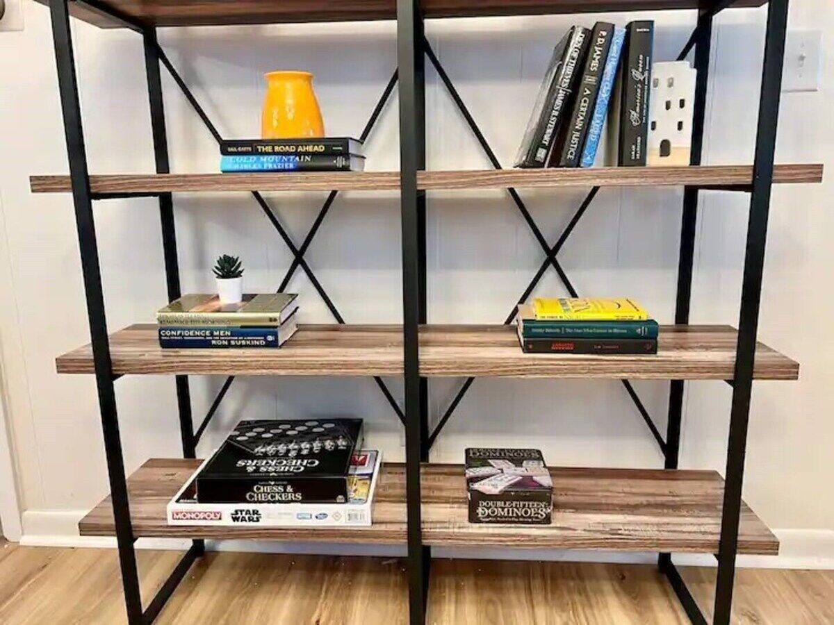 Una estantería de madera con varios estantes que albergan libros, juegos de mesa y una planta pequeña.