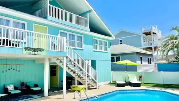 A two-story house with a swimming pool, outdoor seating, and a staircase leading to a balcony. - A Wave From It all - walk to beach - pool! (Holden Beach)