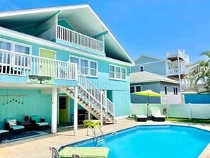 Una casa de dos pisos con piscina, mobiliario exterior y una escalera que conduce a un balcón.