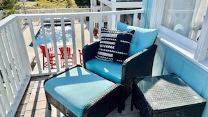 A balcony with a blue cushioned sofa, a small table, and red chairs. - A Wave From It all - walk to beach - pool! (Holden Beach)