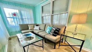 A living room with a sofa, a glass coffee table, and a lamp. - A Wave From It all - walk to beach - pool! (Holden Beach)