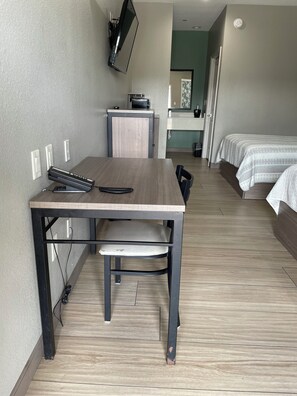 A hotel room with a wooden table, a TV mounted on the wall, a small kitchenette, and two beds with white bedding. - Express Inn - Richey (Houston)