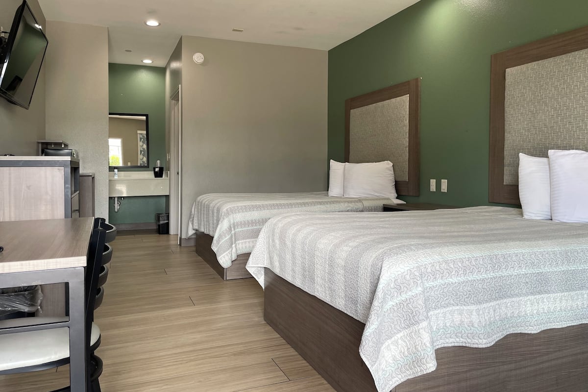 A hotel room with two beds, a desk, a TV, and a bathroom visible through an open door.