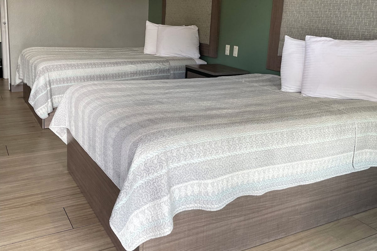 A hotel room with two beds, each with a wooden headboard, a small bedside table, and a wall-mounted mirror.