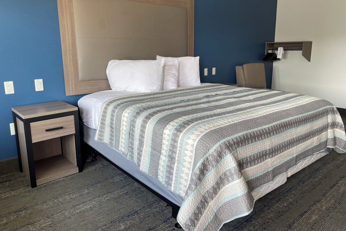 A hotel room with a bed, a nightstand, a wall-mounted lamp, and a blue wall.