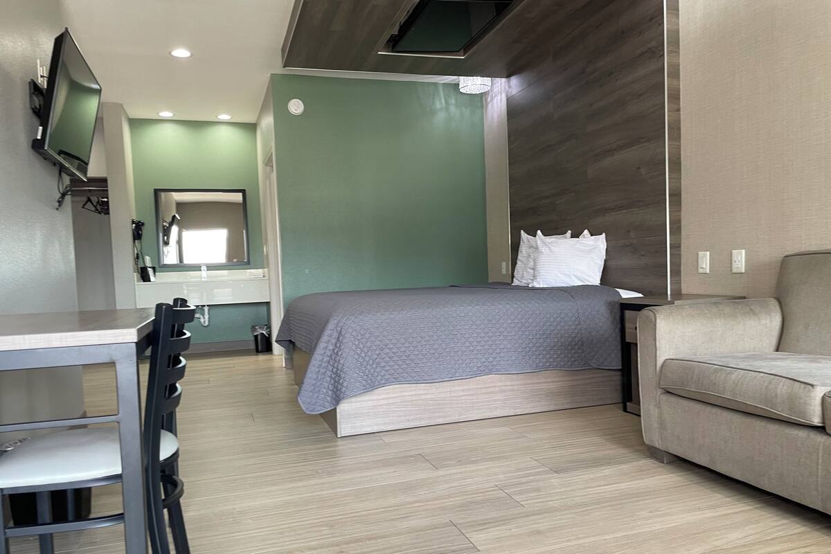A modern hotel room with a bed, a sofa, a desk, and a TV mounted on the wall.