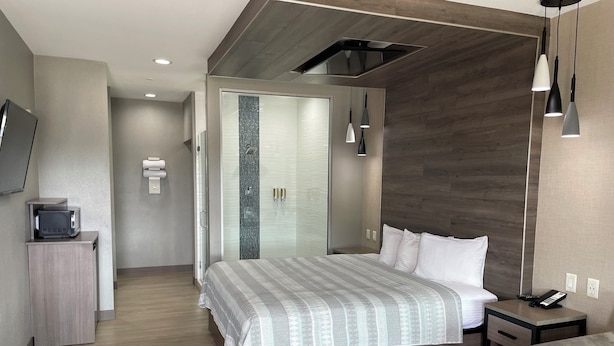 Una habitación de hotel moderna con cama, mesita de noche y televisor en un mueble.