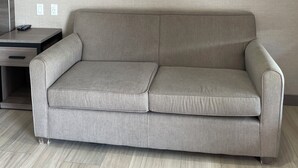 Un sofá de tonos neutros frente a una pared lisa, una mesita auxiliar con un control remoto y una lámpara de araña moderna.