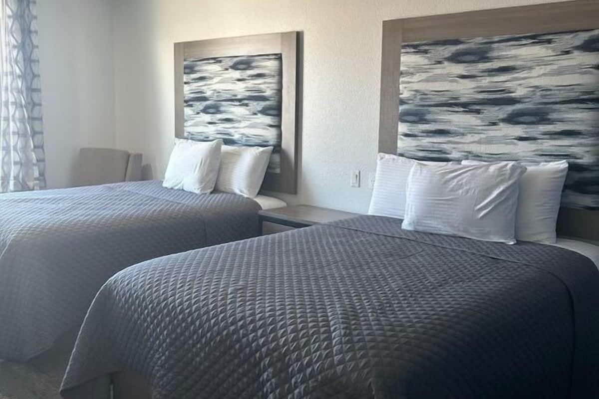 A hotel room with two beds, a large window with curtains, and abstract artwork on the walls.