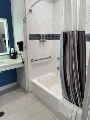 A modern bathroom with a white bathtub, a shower with a curved door, a hand dryer, and a towel rack. - Express Inn - Richey (Houston)