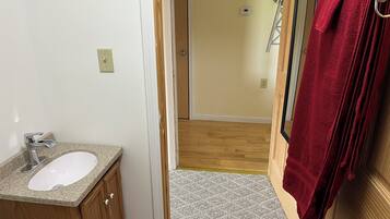 Un baño con lavamanos blanco, mueble de madera y una toalla roja colgada en la puerta.