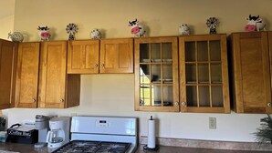 Una cocina con armarios de madera, una estufa, un rincón para café y figuritas decorativas de vacas en los armarios superiores.