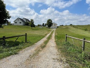 A gravel path leading to a white house with a garage, surrounded by grassy fields and trees. - Charming 2-bedroom cottage with WiFi, AC in peaceful Middlebury (Middlebury)