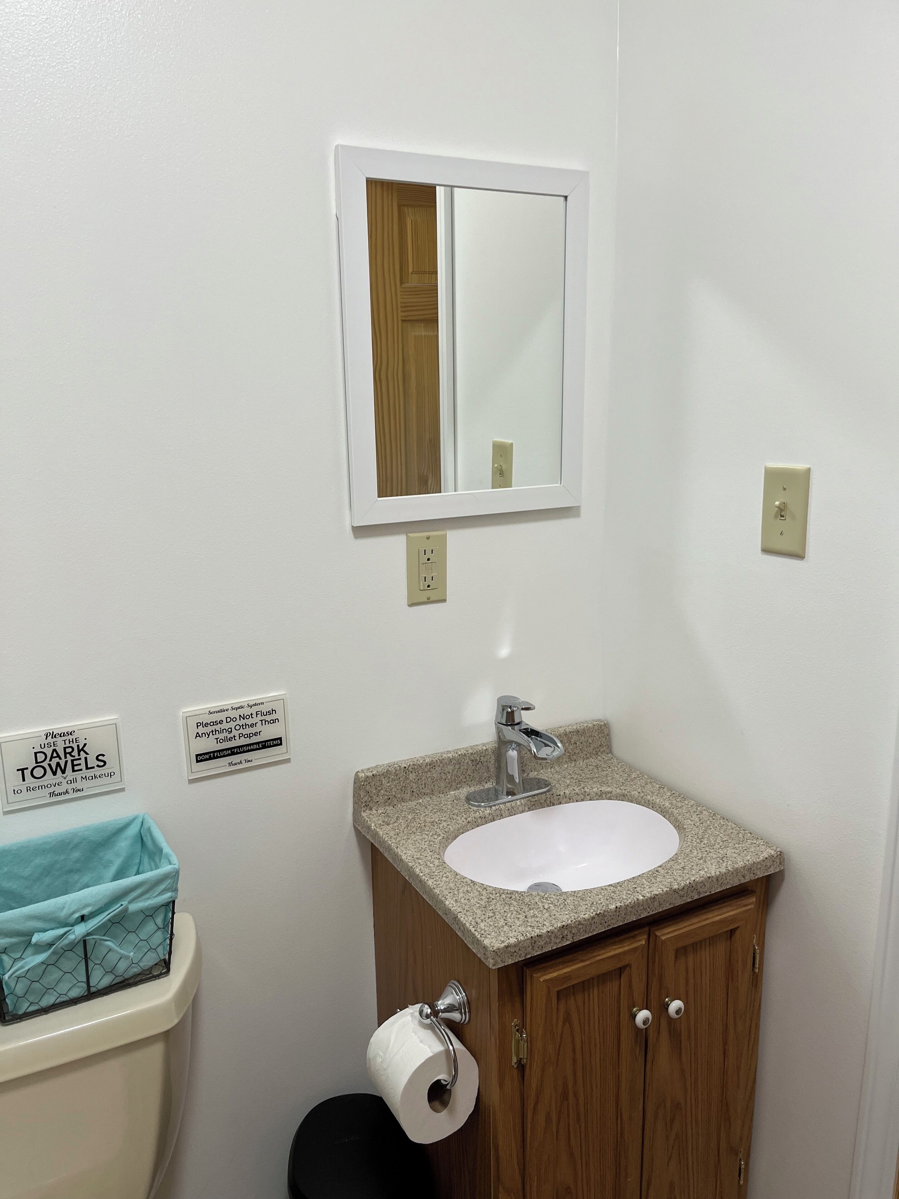 A bathroom with a sink, mirror, toilet paper holder, and a sign about using dark towels.
