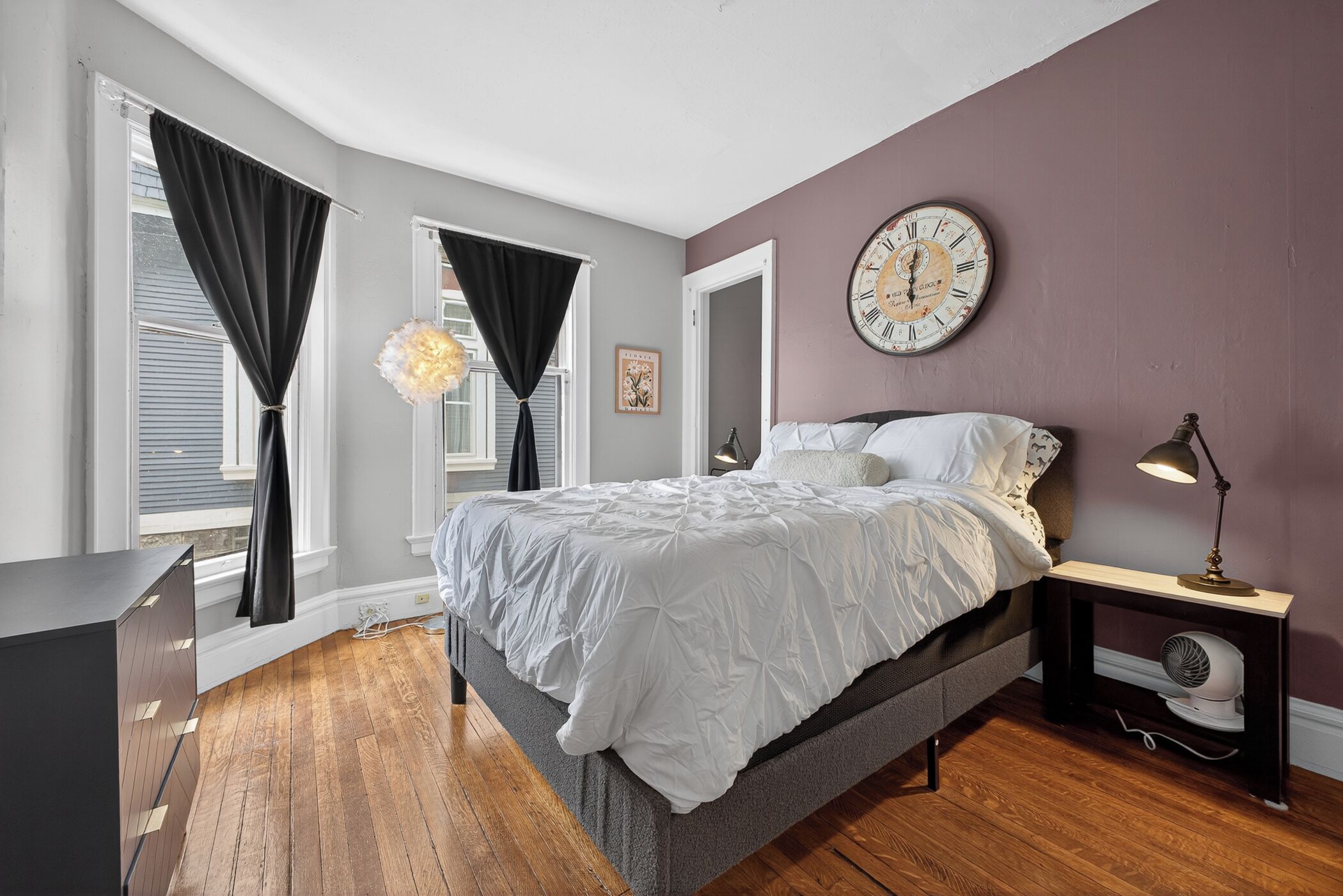 A bedroom with a bed, a clock, a nightstand, and a window with curtains.
