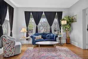 Una sala de estar moderna con un sofá azul, un sillón estampado, una mesa redonda de centro, un tapiz con diseño y una planta en maceta.