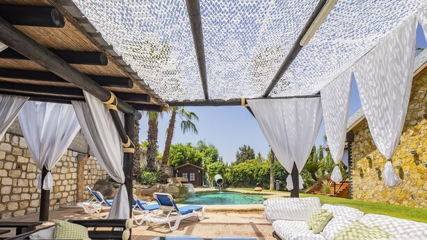 Un espace aménagé au bord de la piscine, avec des chaises longues, une table en verre et un coin salon couvert doté de coussins.