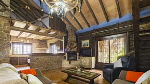 Un intérieur rustique avec des murs en pierre, des poutres en bois, une cheminée en pierre, un téléviseur et un coin repas.