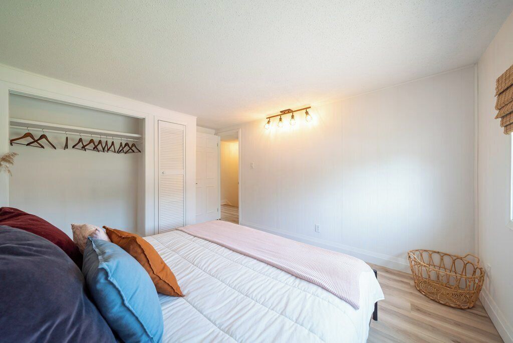 Een slaapkamer met een bed, een kledingkast, een hanglamp en een rieten mand.