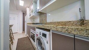 Een compacte keuken met een ingebouwde wasmachine en droger, een granieten aanrechtblad en witte kastjes.