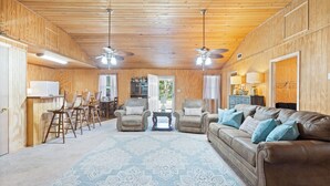 A spacious living room with a brown leather sofa, two armchairs, a patterned rug, and wooden walls.