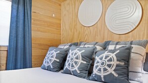 A bed with multiple pillows, a wooden wall, and a window with curtains.