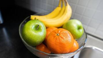 A glass bowl containing green apples, an orange, and a bunch of bananas on a kitchen counter.