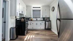 A compact kitchen with white cabinets, stainless steel appliances, and a wooden floor. - Outdoor Sauna|Hot Tub|Playroom|Port Dallhousie (St. Catharines)