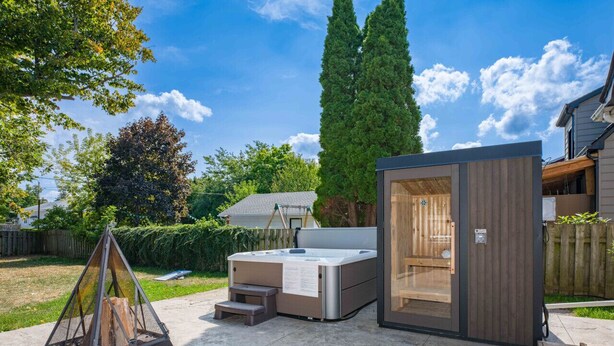 A hot tub with a wooden deck and steps, surrounded by a wooden fence and trees. - Outdoor Sauna|Hot Tub|Playroom|Port Dallhousie (St. Catharines)