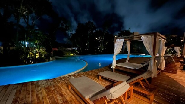 Zona de piscina nocturna con tumbonas de madera y una estructura tipo dosel.