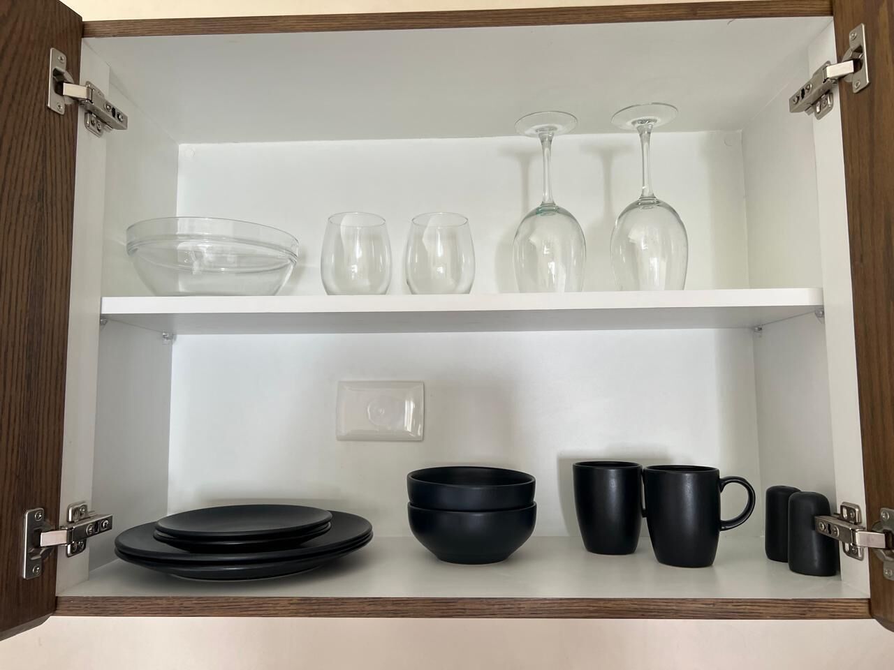 A kitchen cabinet with black and clear glassware, including bowls, plates, and wine glasses.