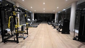 Un gimnasio con equipamiento de ejercicio, suelo de madera y ventanas amplias.