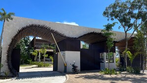 Un edificio moderno con una entrada en arco distintiva, una motocicleta estacionada adelante y un jardín bien cuidado.