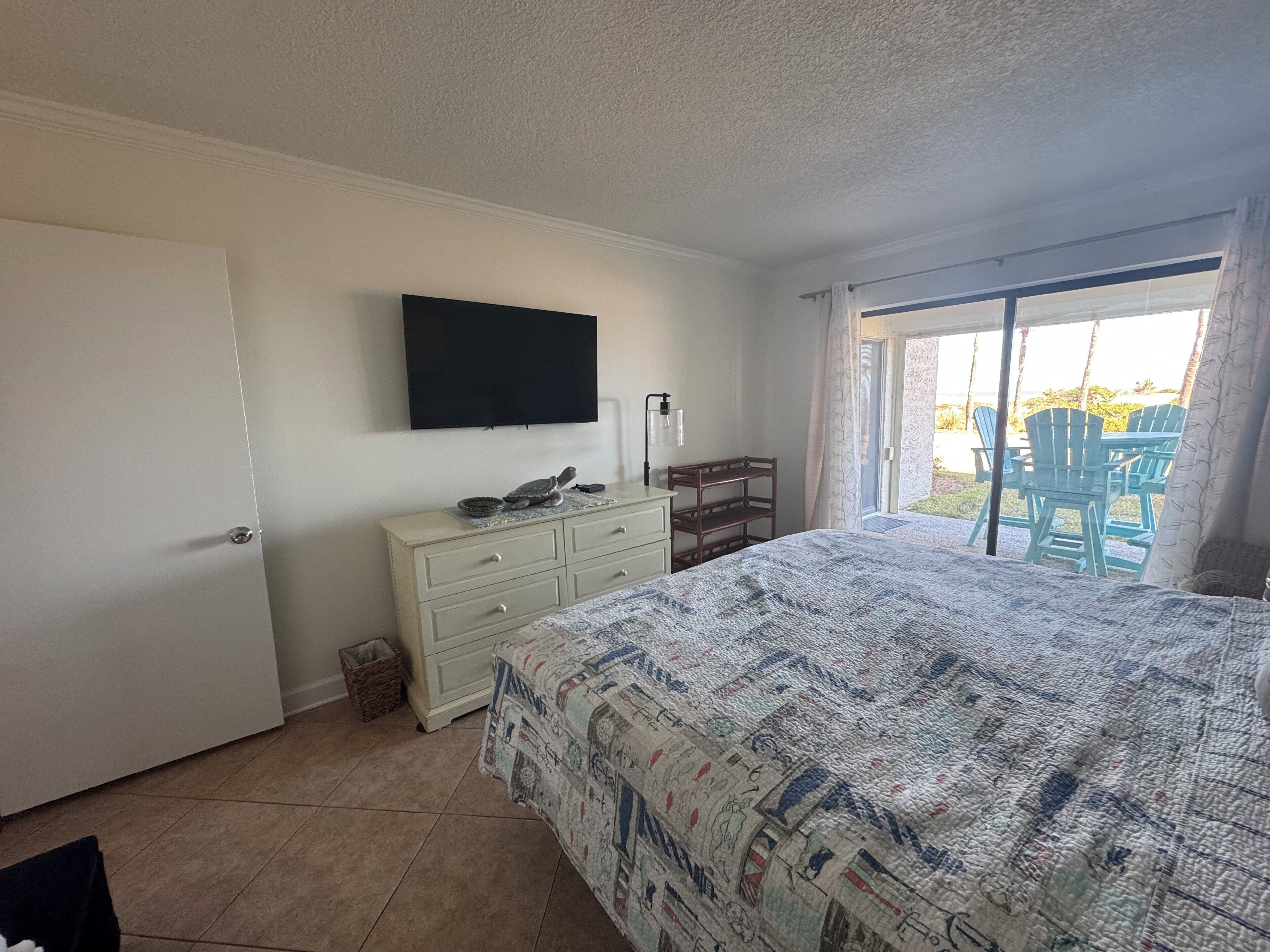 A bedroom with a bed, a dresser, a television, and a balcony with chairs.