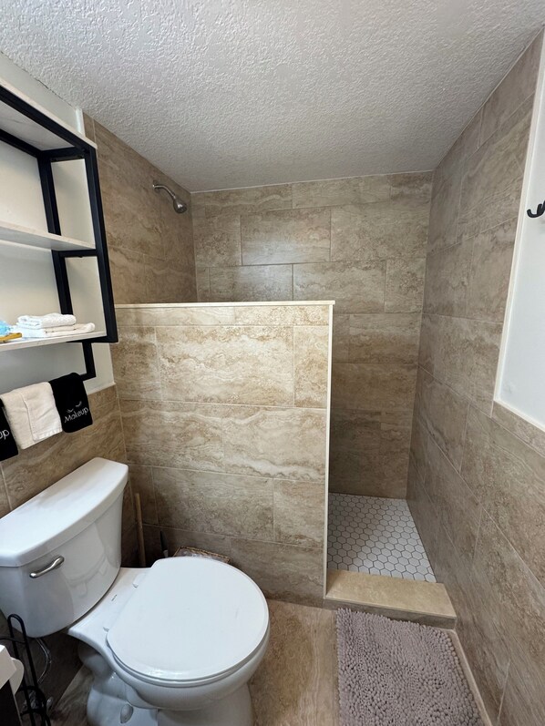 A bathroom with a toilet, a shower enclosure, and a shelf with towels. - Relaxing OceanFront~FirstFloor~Steps to Sand~Pool (Nassau County)