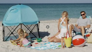 Een gezin op het strand, met een tent, strandspullen en een strandbal.