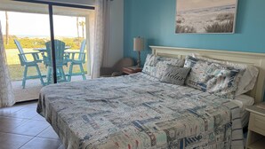 Slaapkamer met een groot bed, uitzicht op de omgeving door een schuifdeur, een stoel en een tafel buiten.