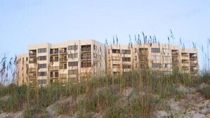 Een meerlaags gebouw met een gelijkmatig gevelontwerp, omgeven door zandgrond en schaarse begroeiing.