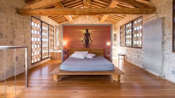 Un dormitorio amplio con una cama grande, vigas de madera, paredes de piedra y vista a un edificio de piedra.