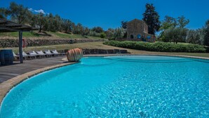 Una piscina azul cristalina con sillas de descanso y un edificio de piedra al fondo.