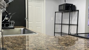 Una cocina con encimeras de granito, un microondas sobre una estantería metálica y una puerta con marco blanco.