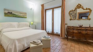 A bedroom with a bed, a nightstand, a dresser, a mirror, and a window with curtains. - Santa Colomba House, Siena, Nature And Pool (Monteriggioni)